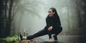 Athletic woman stretching on the road in the misty forest. Copy space.